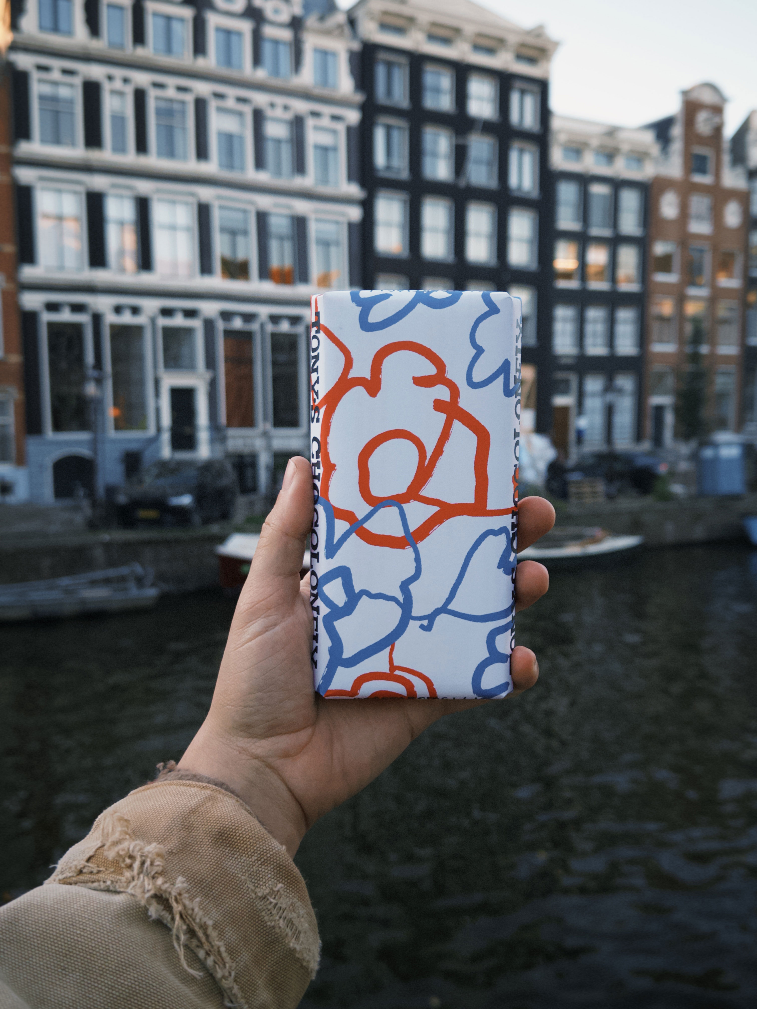 Tony’s Chocolonely packaging design held in hand, Amsterdam canal background, custom illustrated wrapper