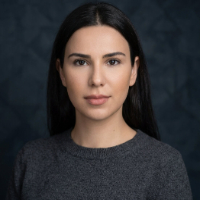 Düz siyah saçlı, gri kazak giymiş genç kadın, koyu arka planda kameraya bakıyor.