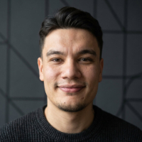 Gülümseyen, siyah saçlı ve siyah kazak giymiş genç adam portresi.