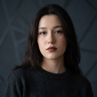 Koyu saçlı, koyu renk kazak giymiş düşünceli genç kadın, koyu renk arka planda.