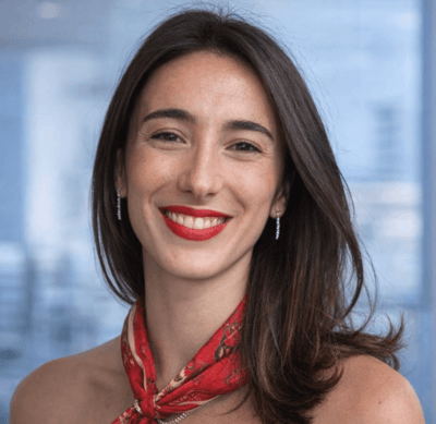 Uzun kahverengi saçlı, kırmızı ruj sürmüş ve kırmızı desenli fular takan gülümseyen kadın portresi.