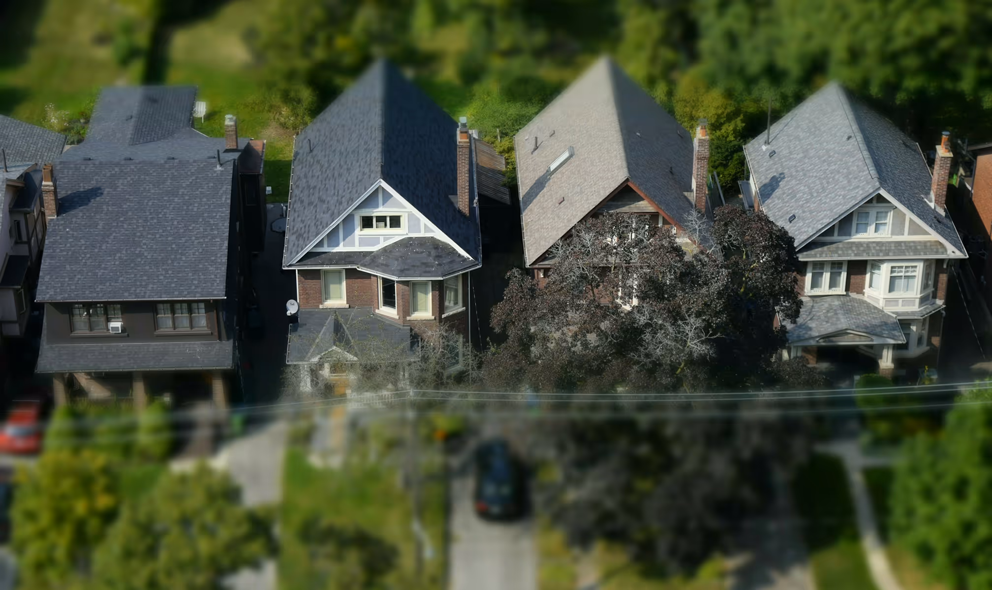 Aerial view of a row of four suburban houses with pitched roofs and surrounding greenery.