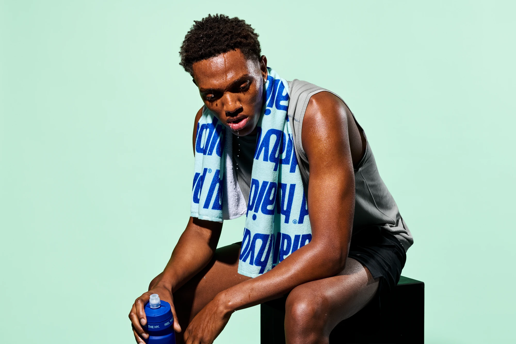 Lifestyle-Fotografie für Hydraid: Sportler mit Markenhandtuch und Trinkflasche, erschöpft nach dem Sport - Lifestyle photography for Hydraid: exhausted athlete holding a water bottle after training