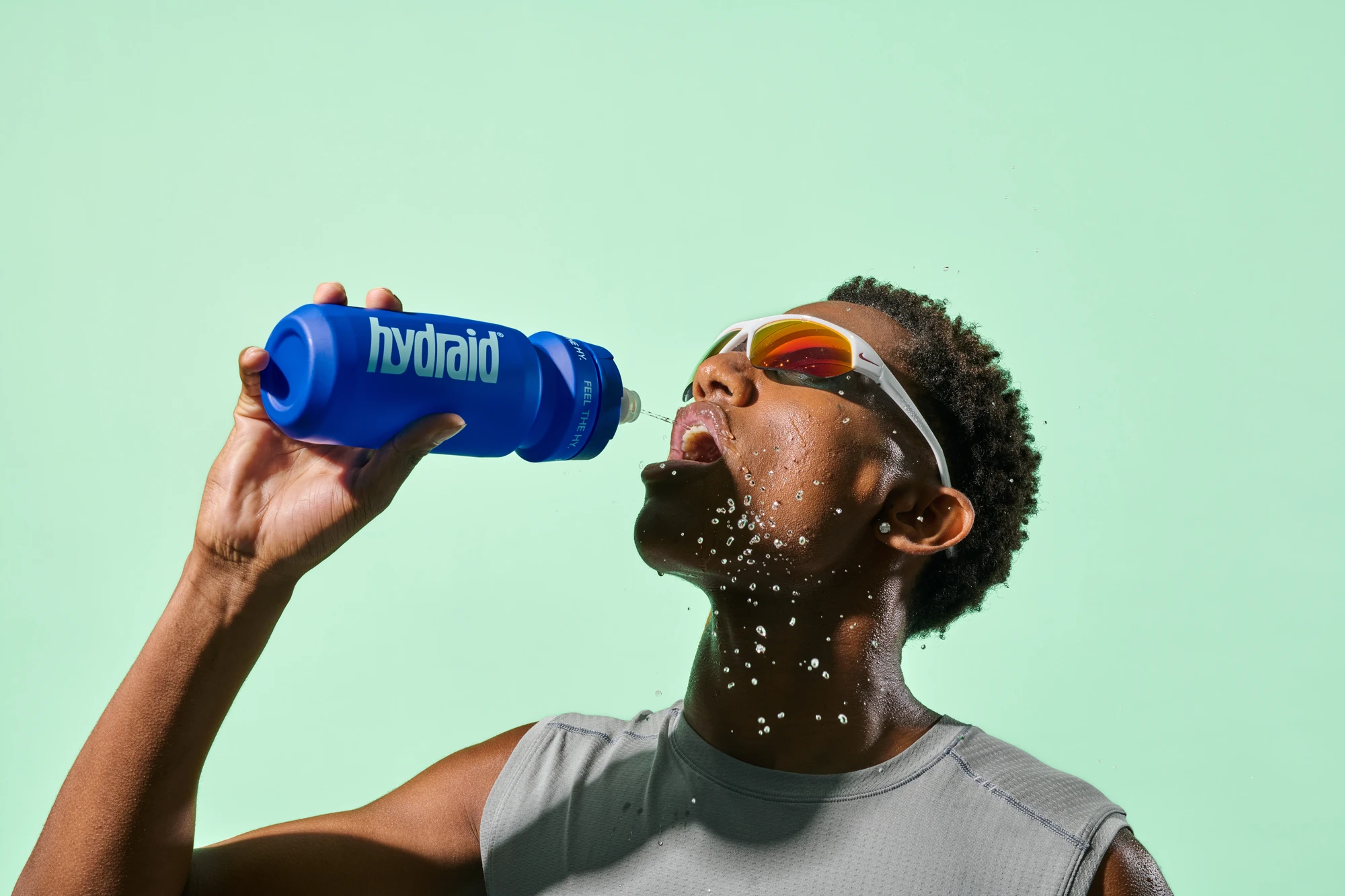 Sportfotografie für Hydraid: Athlet trinkt aus blauer Sportflasche, Wassertropfen im Gesicht Sports photography for Hydraid: athlete drinking from a blue sports bottle with water splashing on his face