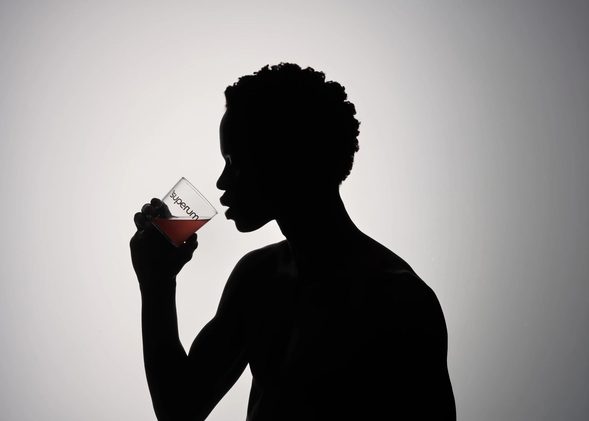 Kunstfotografie für Superum: Silhouette einer Person trinkt aus Markenglas im Gegenlicht | Artistic photography for Superum: silhouette of a person drinking from a branded glass, backlit