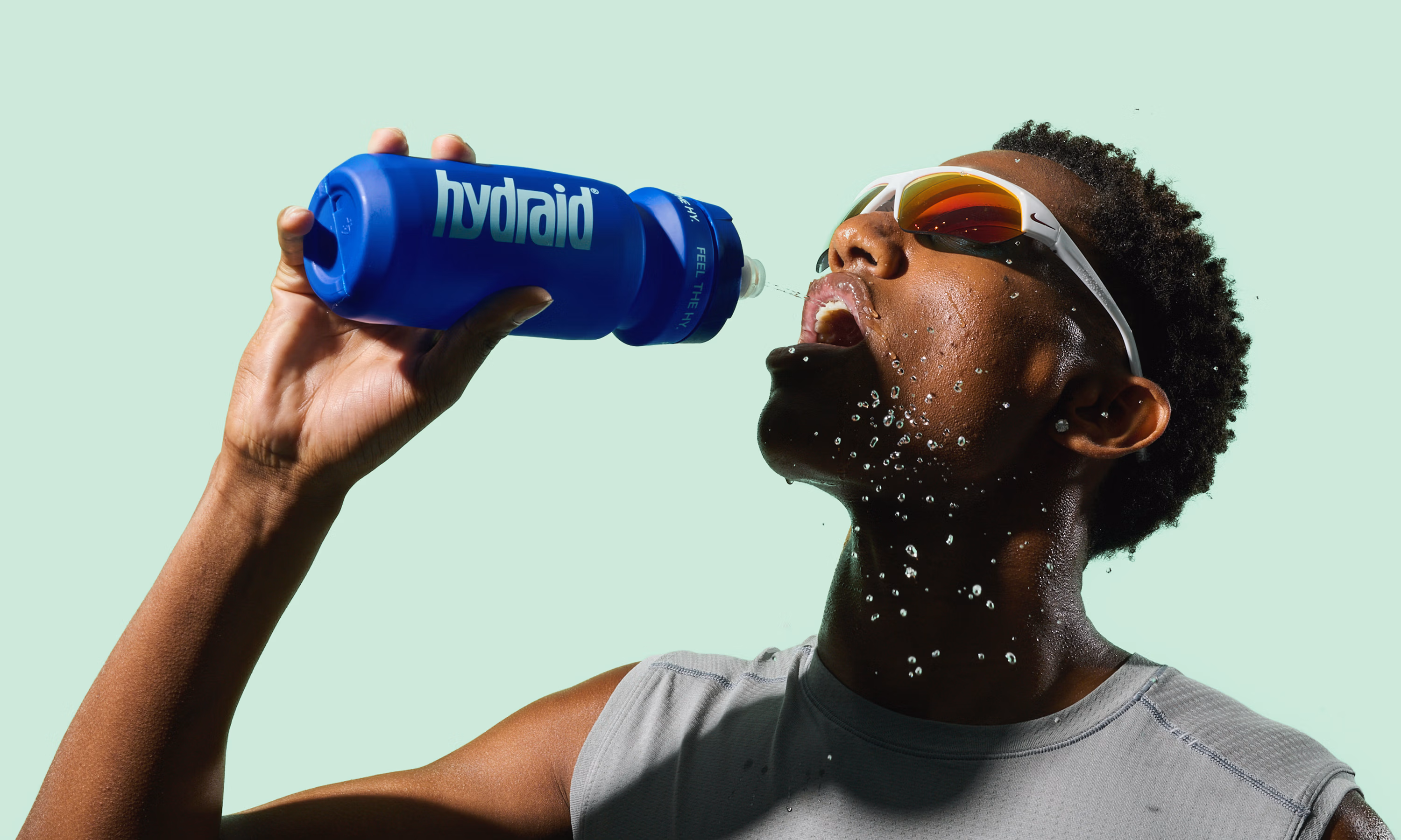 Sportfotografie für Hydraid: Athlet trinkt aus blauer Sportflasche, Wassertropfen im Gesicht Sports photography for Hydraid: athlete drinking from a blue sports bottle with water splashing on his face