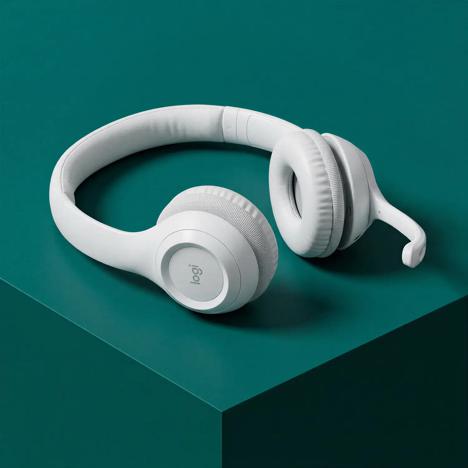 White over-ear wireless headphones with a built-in microphone placed on a teal-colored corner table.