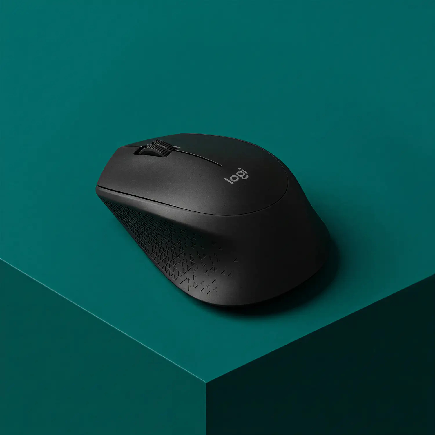 Black wireless Logitech computer mouse on a teal surface.