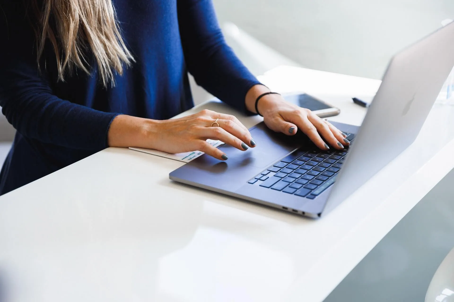 A woman typing on a laptop. Her royal-blue nails match her top.