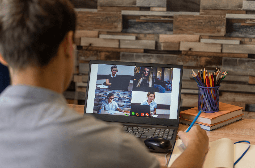Person viewed from behind taking notes while attending a Zoom video call with four colleagues on a laptop