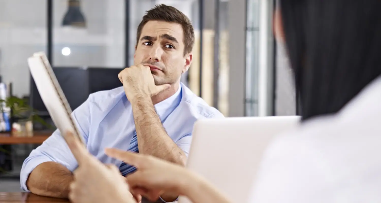 Recruiter holding a resume listens skeptically during a job interview with a candidate across the table