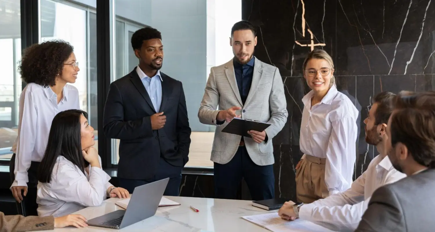 Diverse group of six professionals in a collaborative meeting, with a manager holding a clipboard and leading discussion.