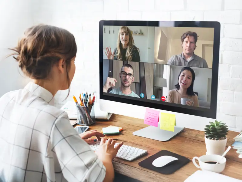 Woman working from home at a desktop computer on a video call with four international colleagues displayed on screen