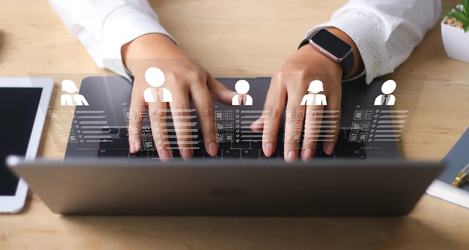 Hands type on a laptop keyboard with a digital overlay showing five silhouetted employee profile icons with linked data cards floating above the screen. A tablet and smartwatch are also visible on the desk, illustrating a direct hire platform used to identify, screen, and onboard elite offshore talent globally.