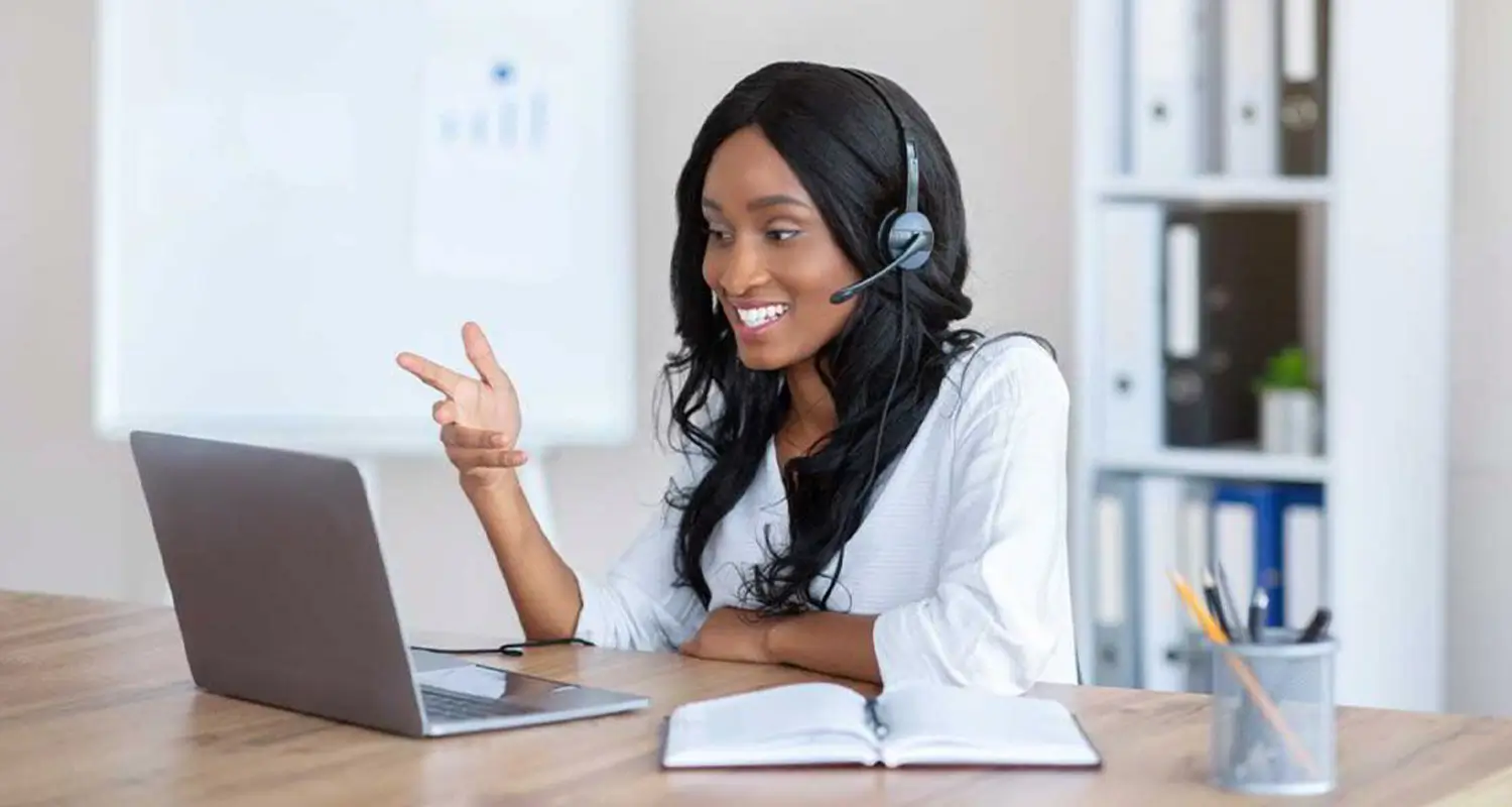 Female virtual assistant wearing a headset gesturing during a video call on a laptop