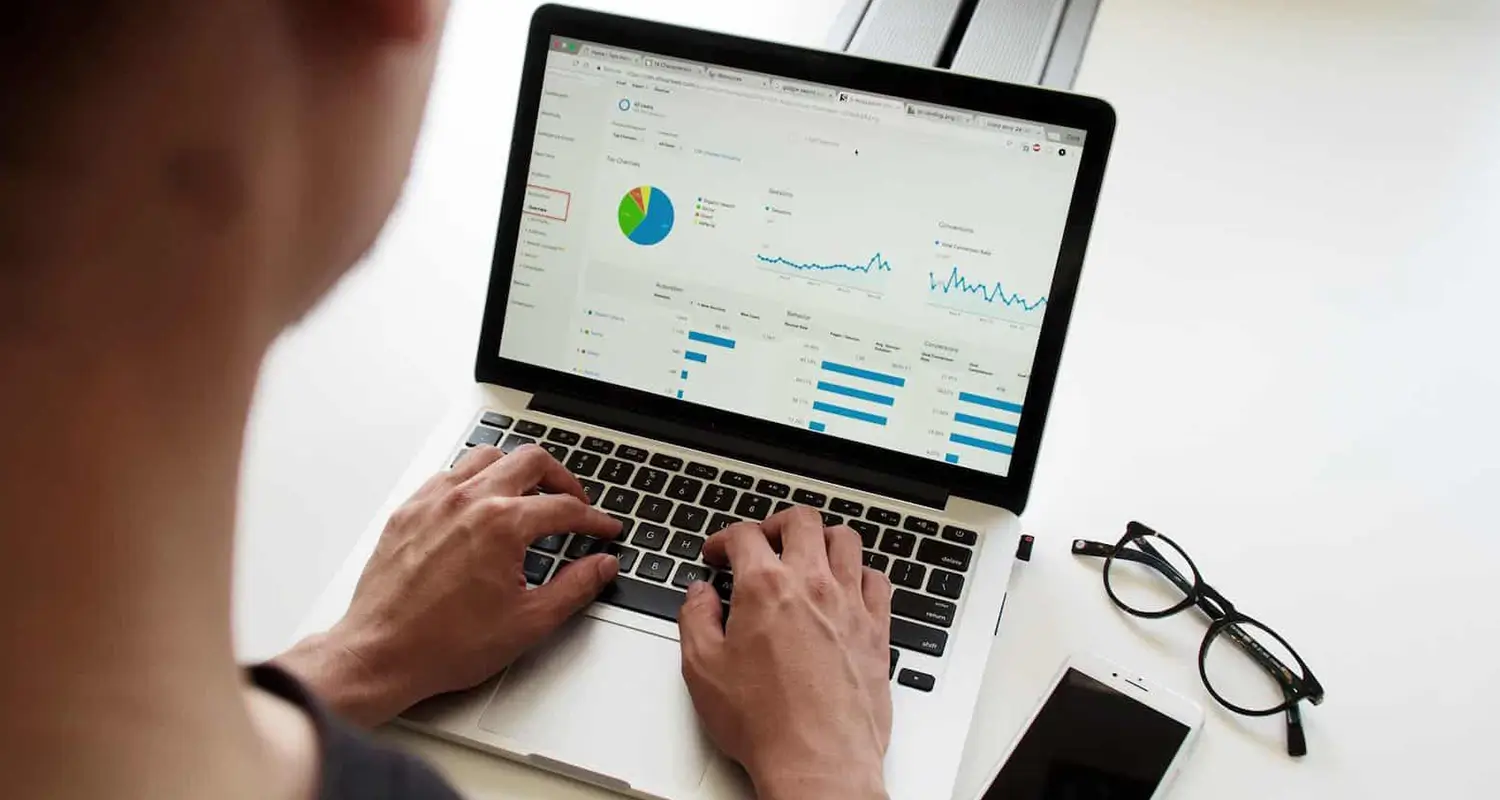 Person typing on a laptop displaying an analytics dashboard with charts and graphs