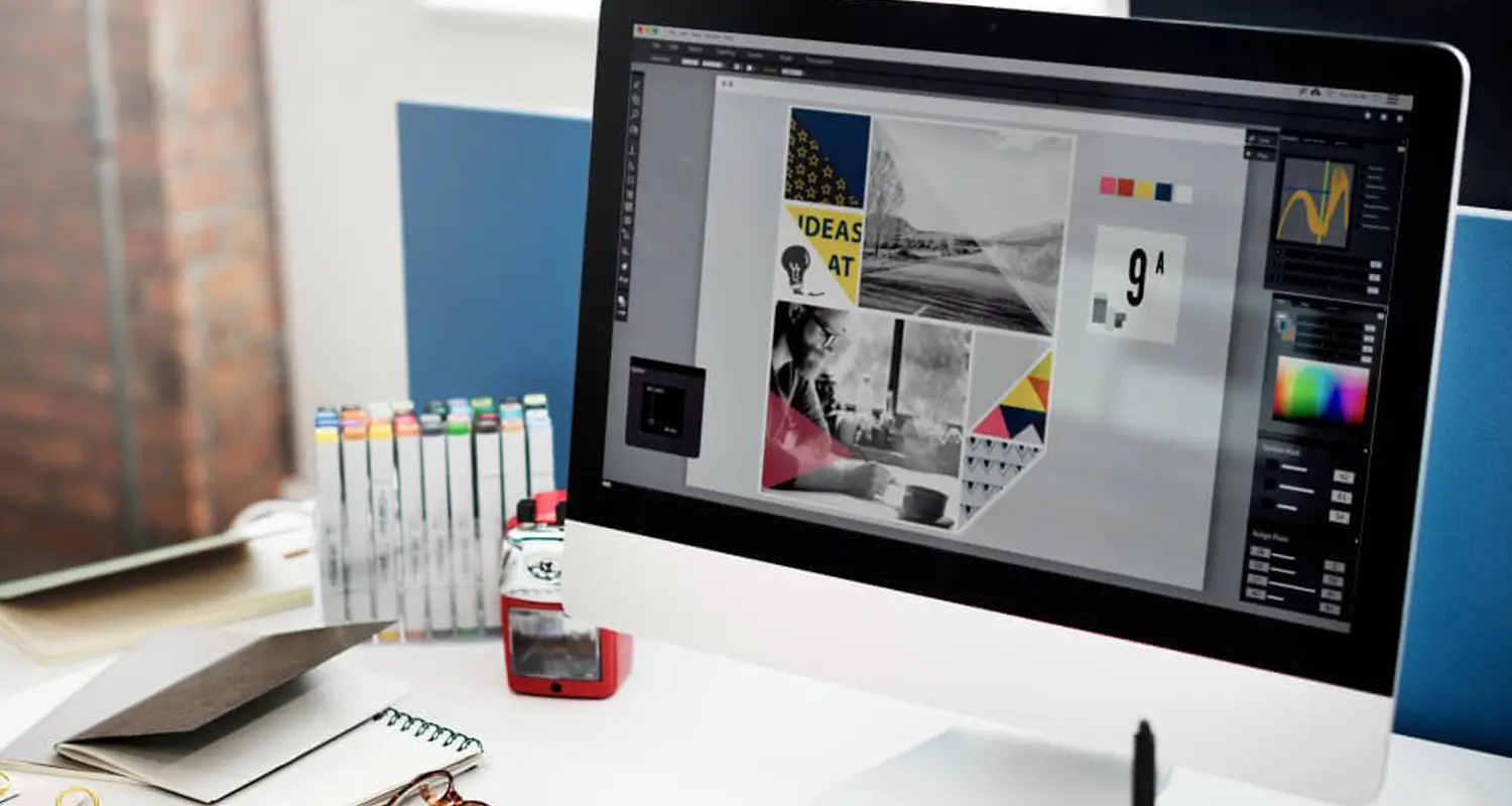 An iMac on a bright design studio desk displays an Adobe Illustrator workspace with a mood board layout featuring black-and-white photography, bold typography, and color swatches. Marker pens, a notebook, glasses, and a small camera are arranged around the workstation.
