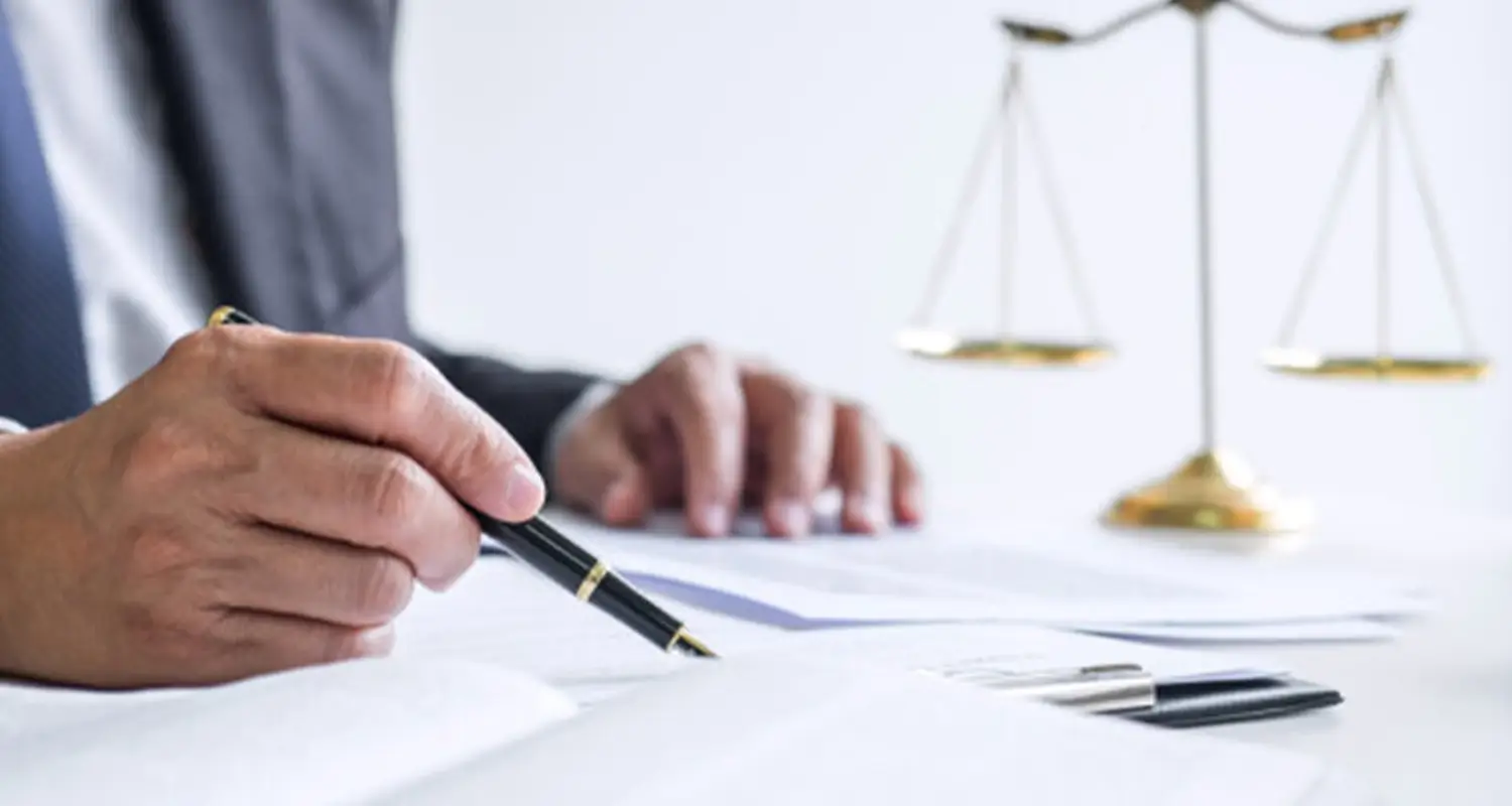 Paralegal reviews and signs legal documents at a desk with a gold scales of justice in the background