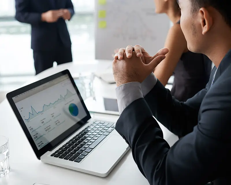 Business professional in a suit reviewing revenue and analytics dashboards on a laptop during a team meeting.
