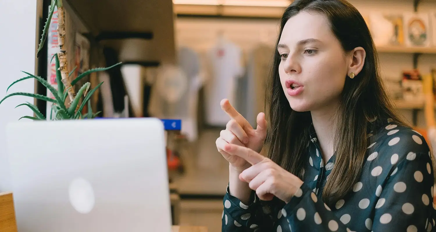 Inventory planner gestures expressively during a video call at her laptop in a retail office setting