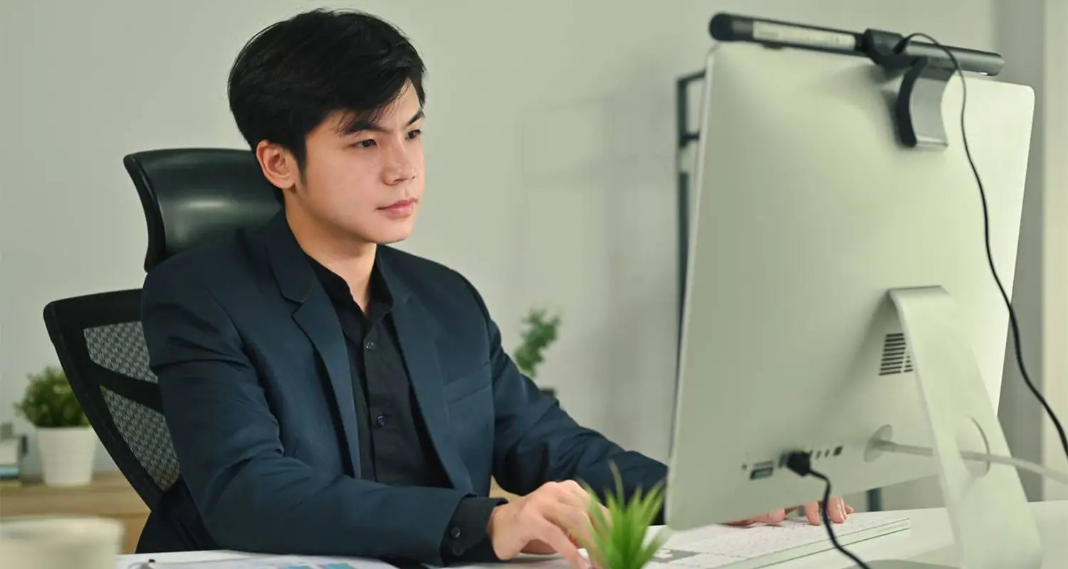 Young professional man in a dark blazer working at a desktop computer in a clean, well-lit modern office