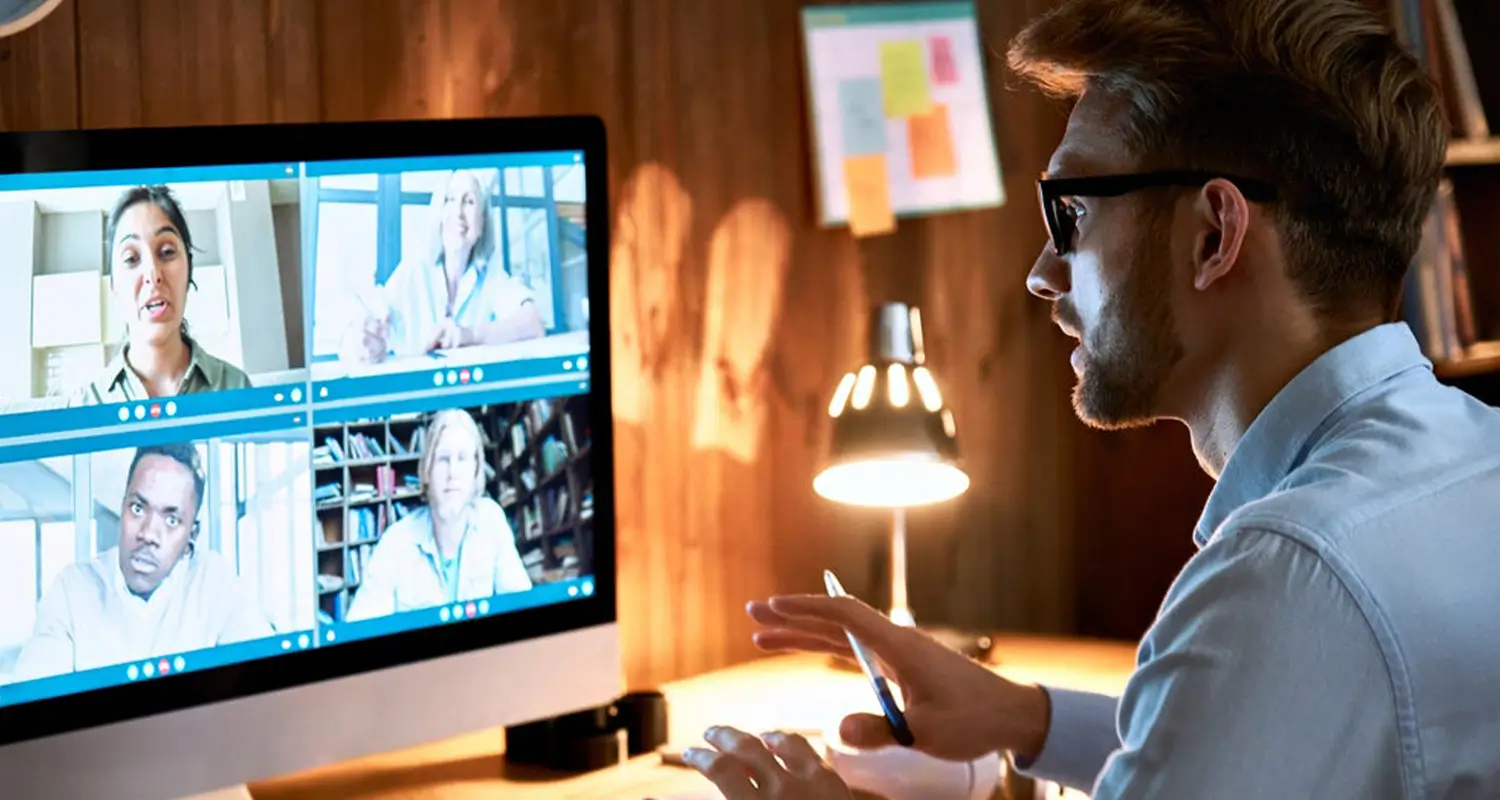 Remote team manager conducts a video call with four distributed team members shown on a large monitor