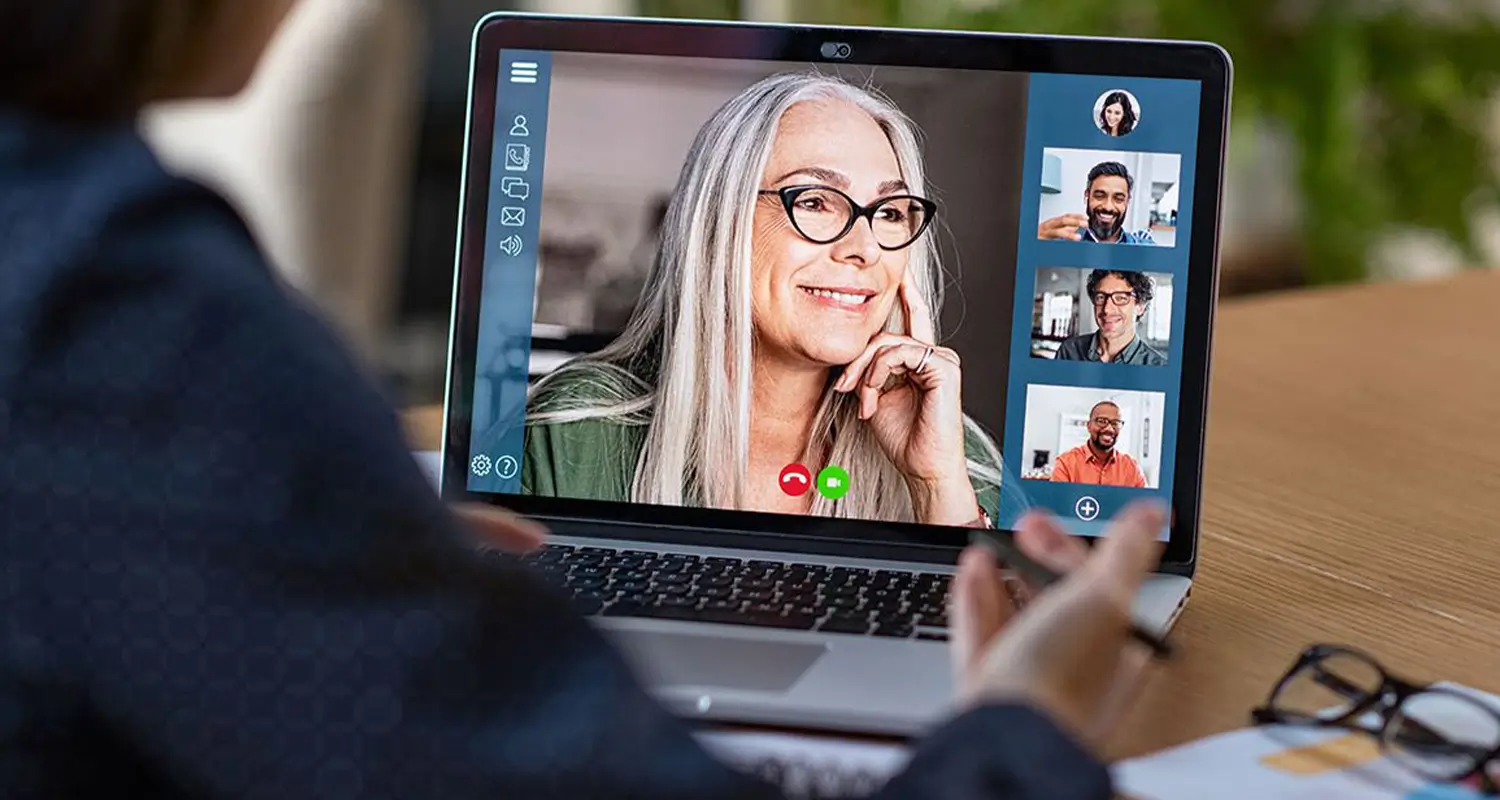 Person views a video conference with a remote team on a laptop, taking notes during a distributed team meeting