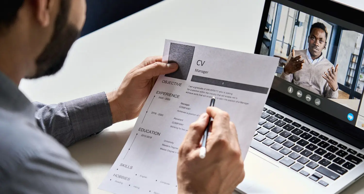 Hiring manager reviews a candidate's CV while conducting a remote video interview on a laptop