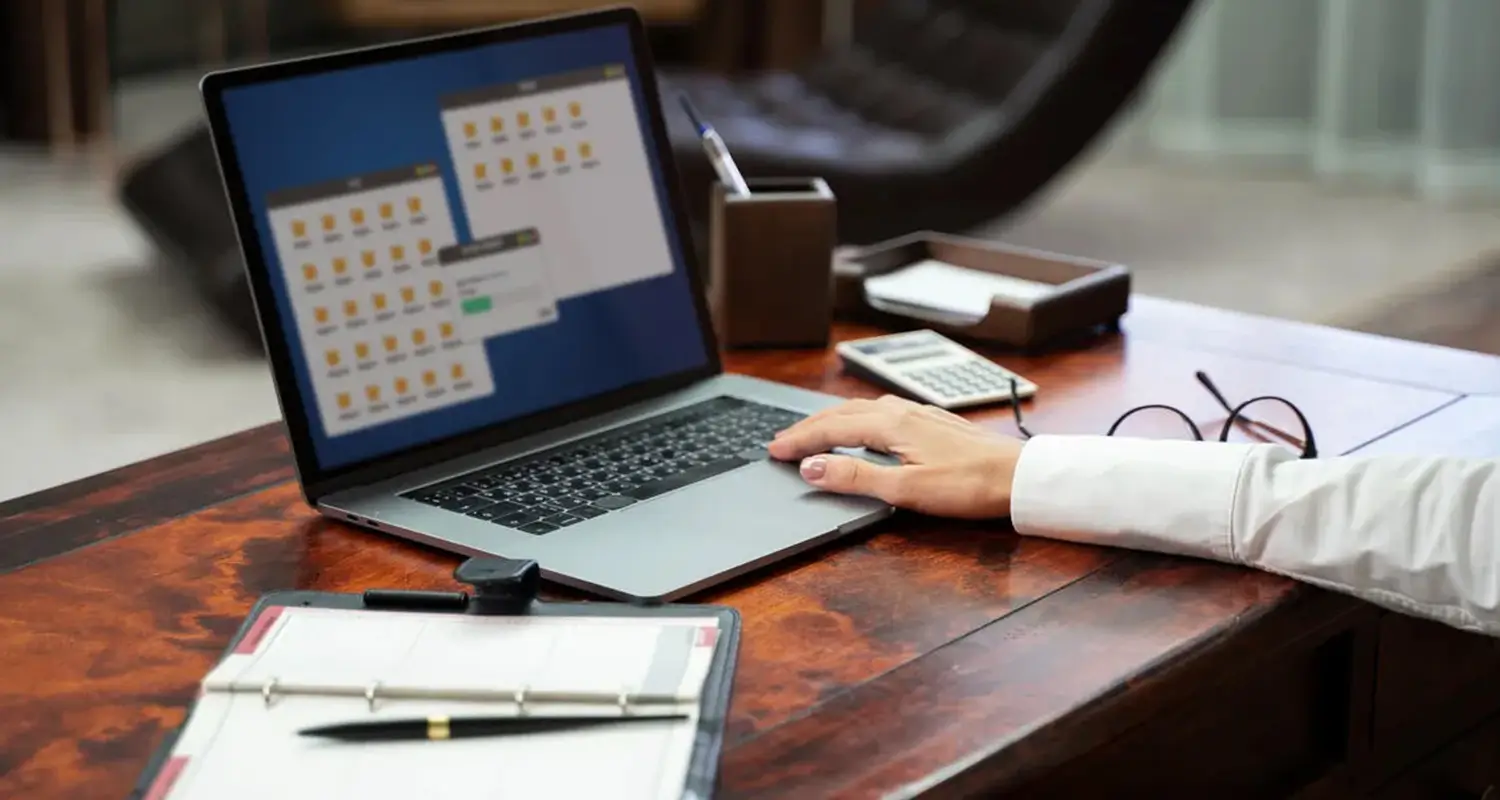 Recruiter browses organized digital folders on a laptop at a wooden desk with a notepad and calculator nearby