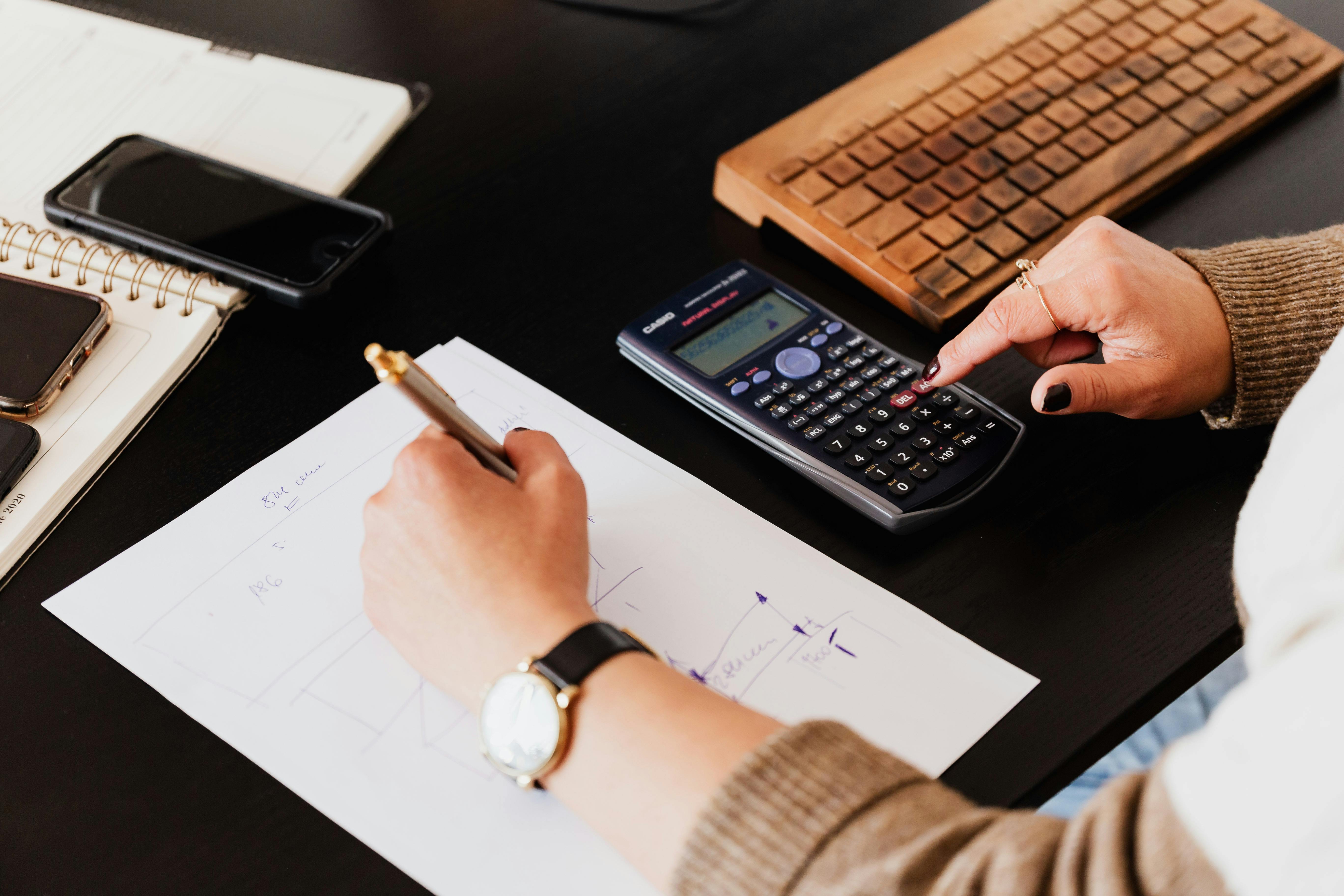 Finance professional using a calculator and writing notes on paper at a desk