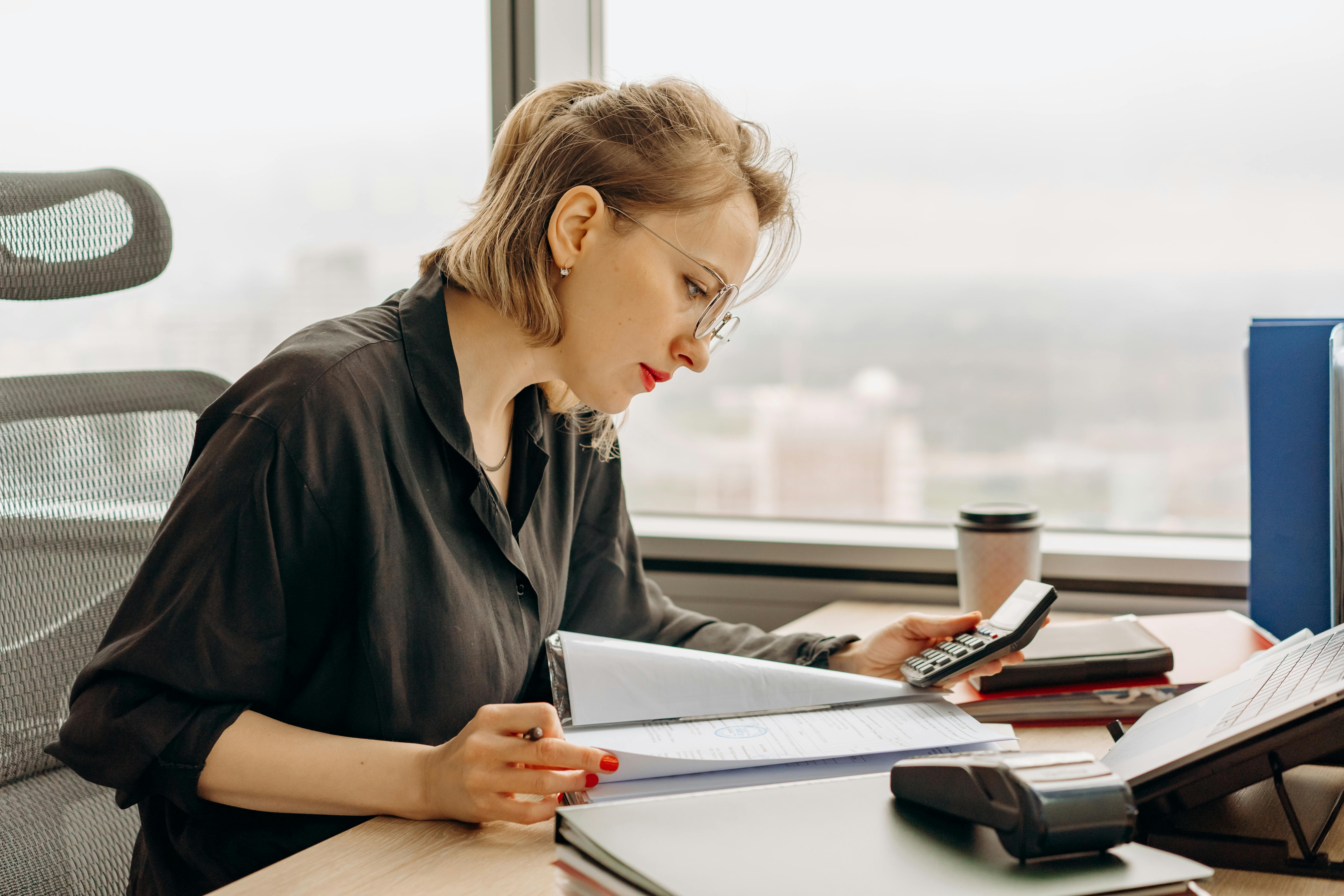 Female finance professional reviewing documents with a calculator in a high-rise office
