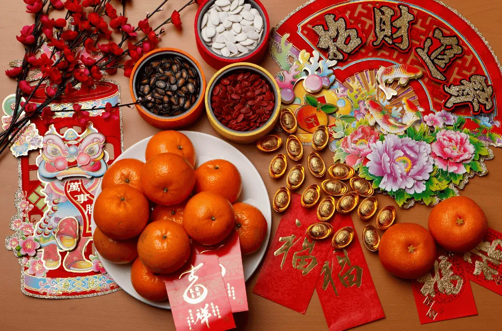 A spread of food, gifts, and items commonly seen in Chinese New Year, from envelopes to oranges.