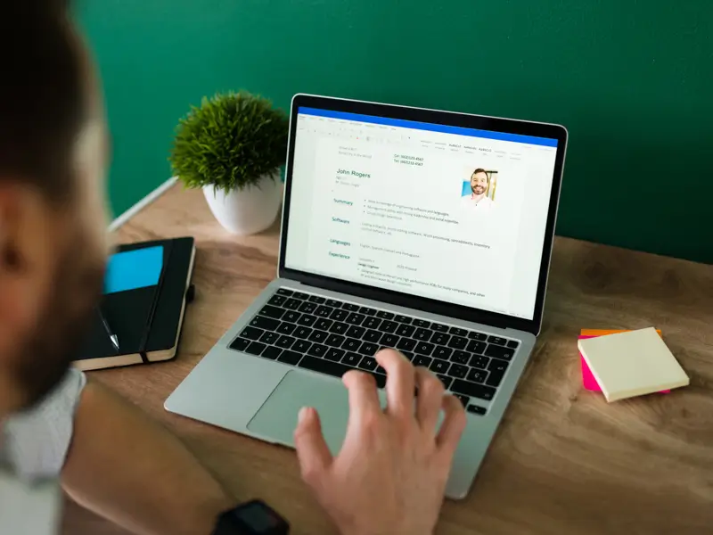 Recruiter reviewing a candidate resume displayed on a laptop screen at a wooden desk with a notebook and sticky notes