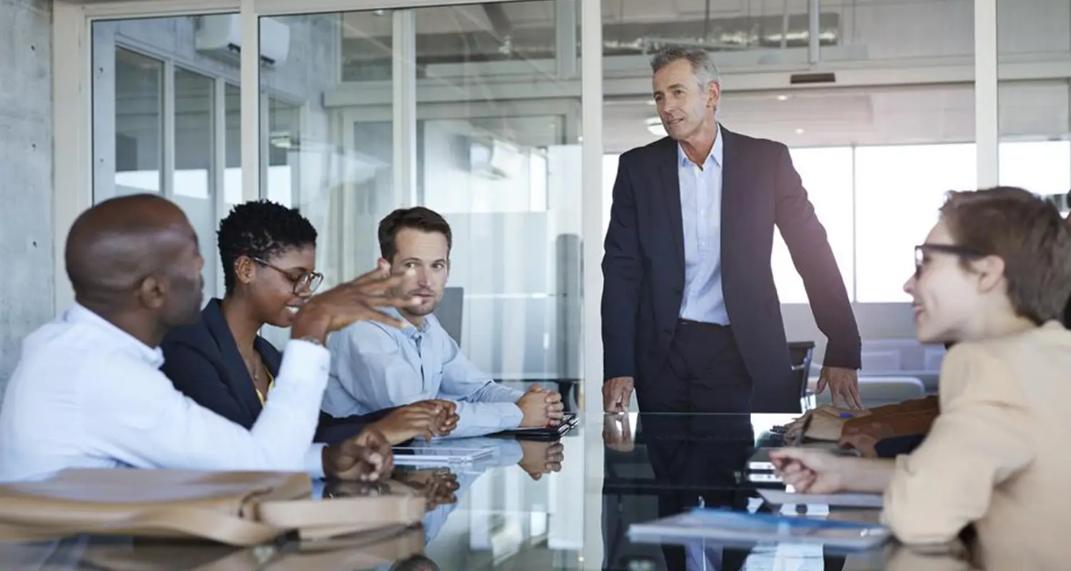 Operations manager leads a cross-functional team meeting in a glass-walled conference room
