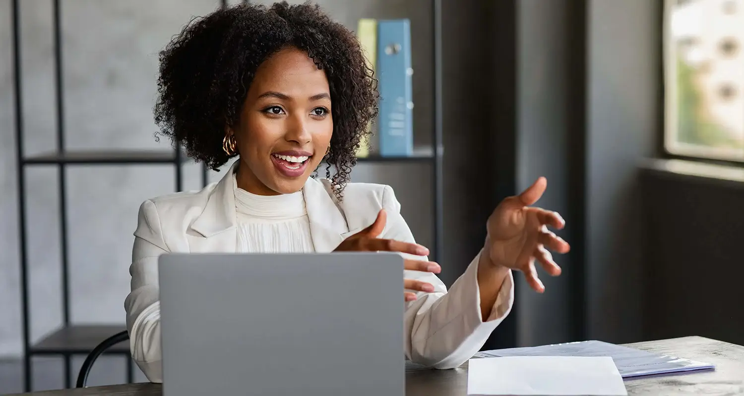 Confident woman in a blazer gestures expressively during a client video call at her desk