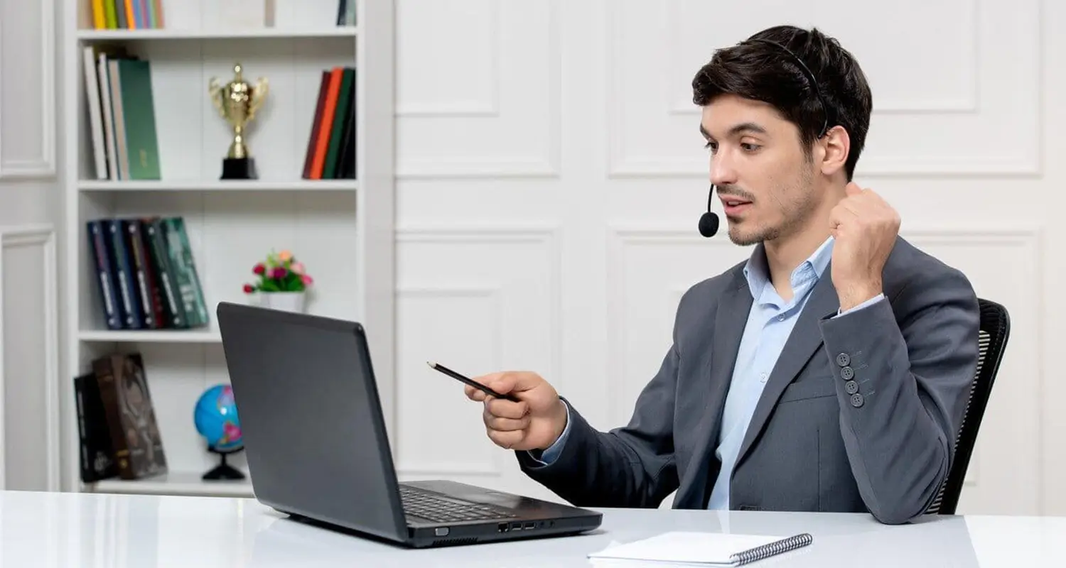 Client relations professional wearing a headset points a pen at a laptop screen during an account review call
