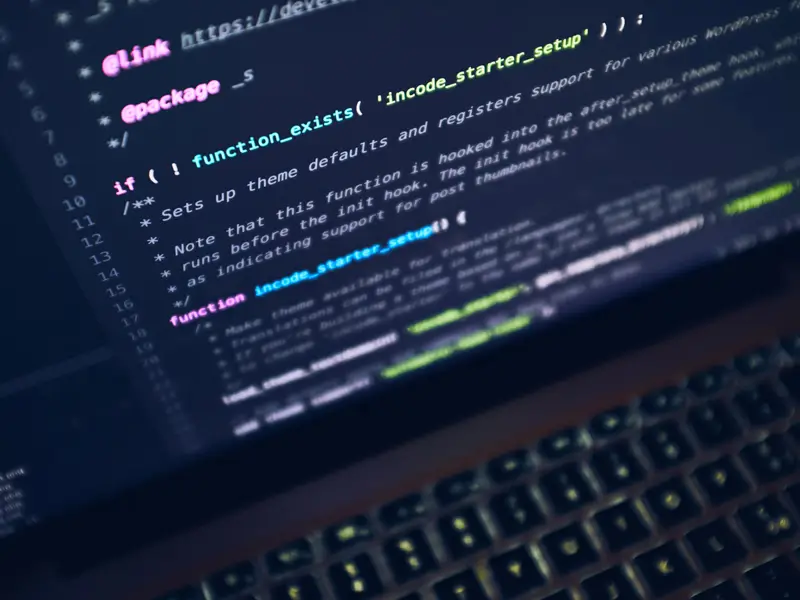 A close-up of a laptop keyboard with a dark code editor on screen showing PHP WordPress theme setup code, with syntax highlighting in pink, green, and white. The angle is tilted, emphasizing the immersive coding environment of an offshore PHP developer.