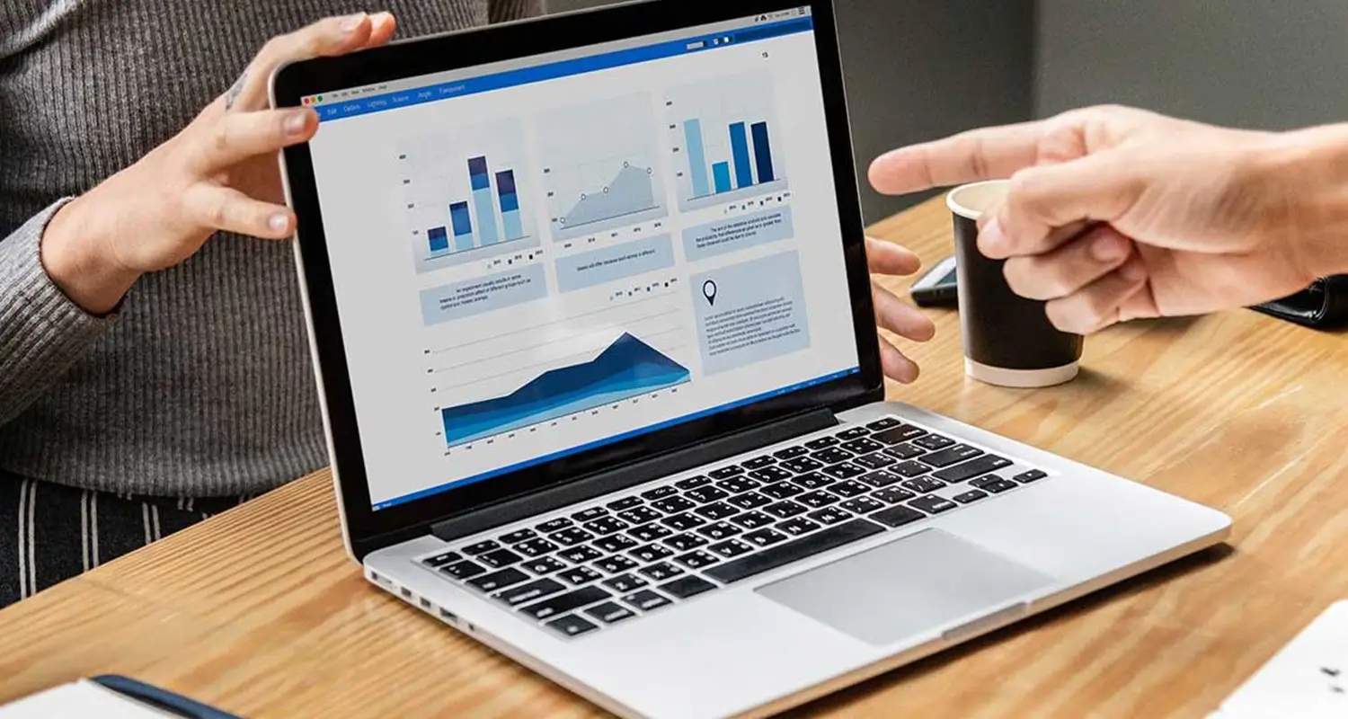 Two colleagues pointing at a laptop displaying a data dashboard with bar and line charts during a strategy meeting