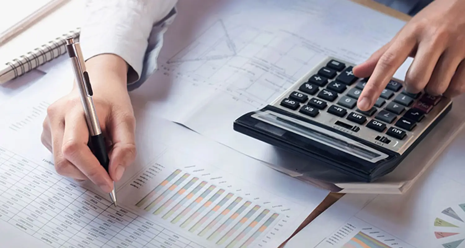 Close-up of hands writing on financial bar chart reports while operating a calculator, reviewing accounts payable data on a desk