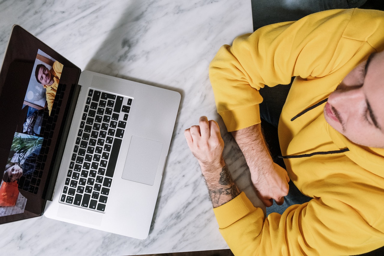 Man in a yellow hoodie participating in a video call on a laptop at a marble table