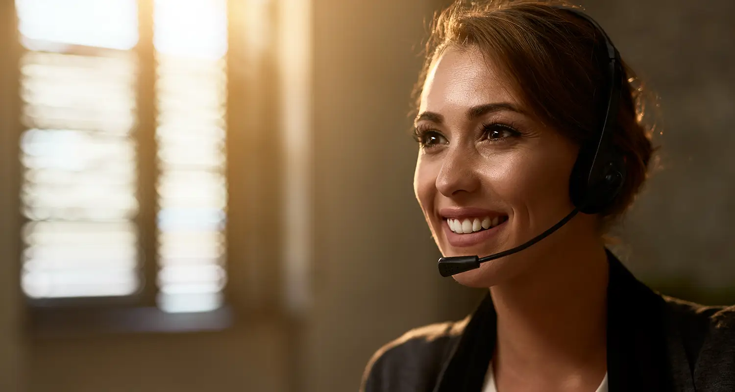 Smiling female client service representative wearing a headset in warm office lighting