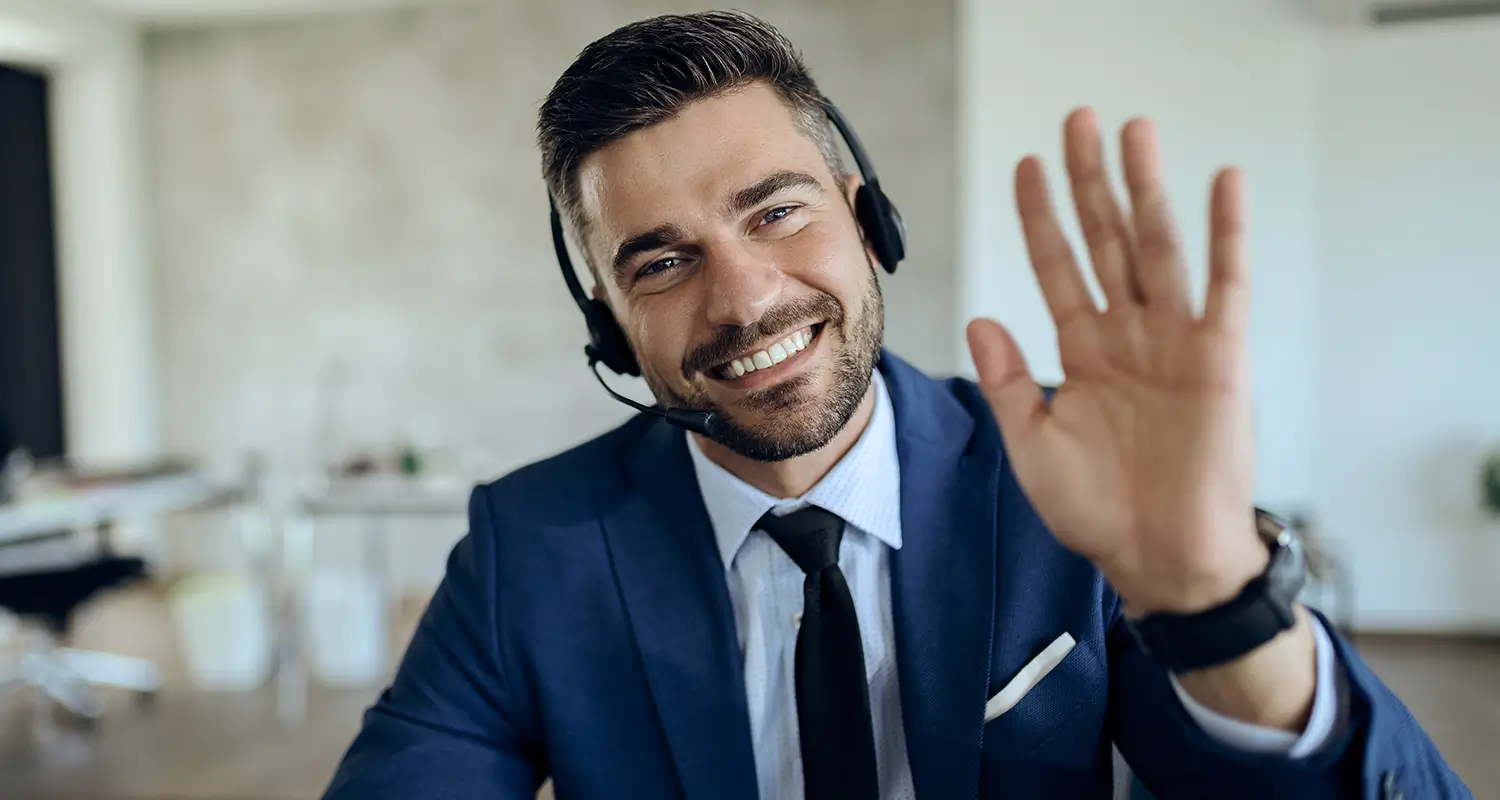 Smiling male client service representative in a suit and headset waving during a call