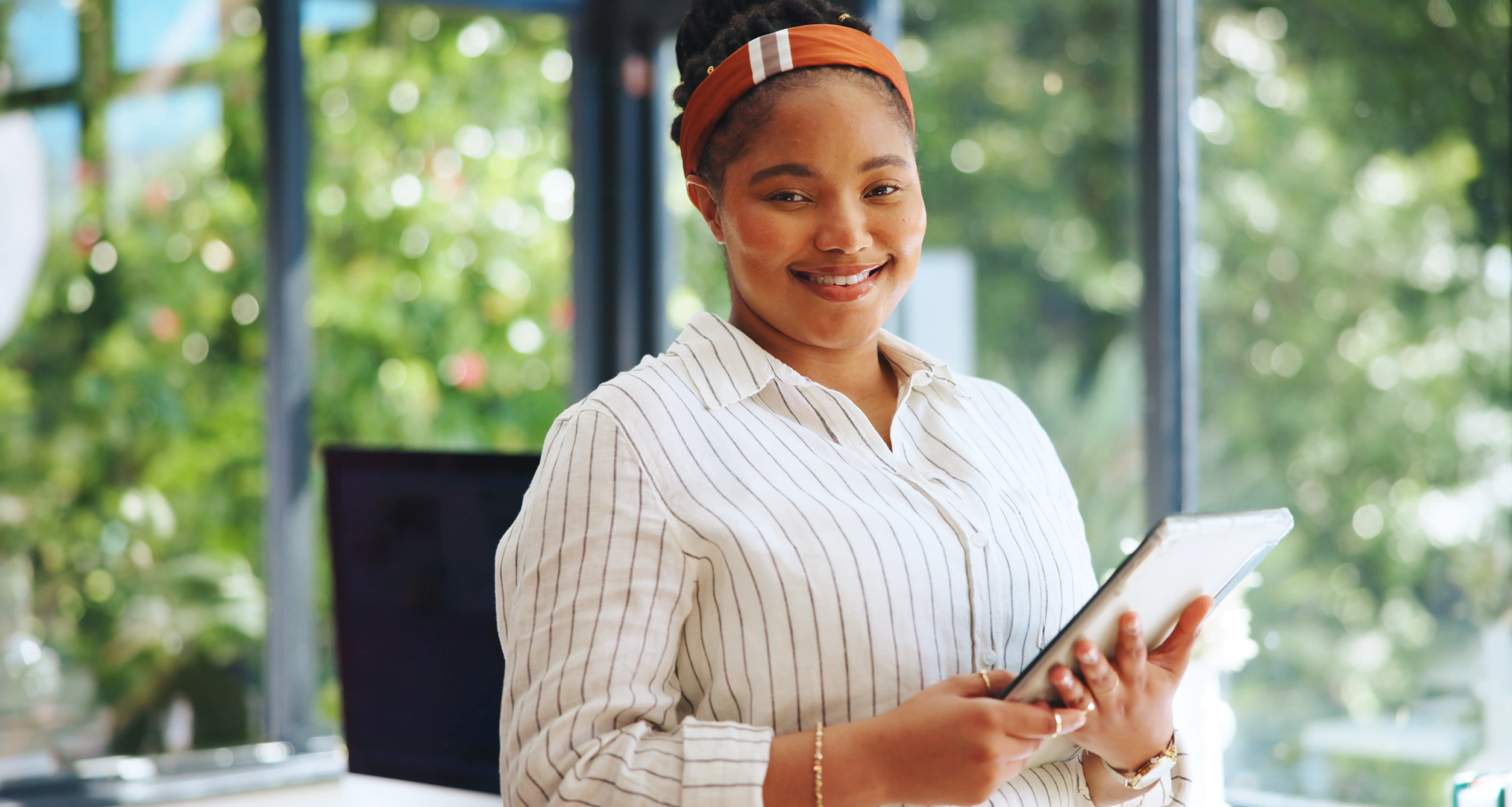 Smiling professional woman holding a tablet in a light-filled office with greenery in the background