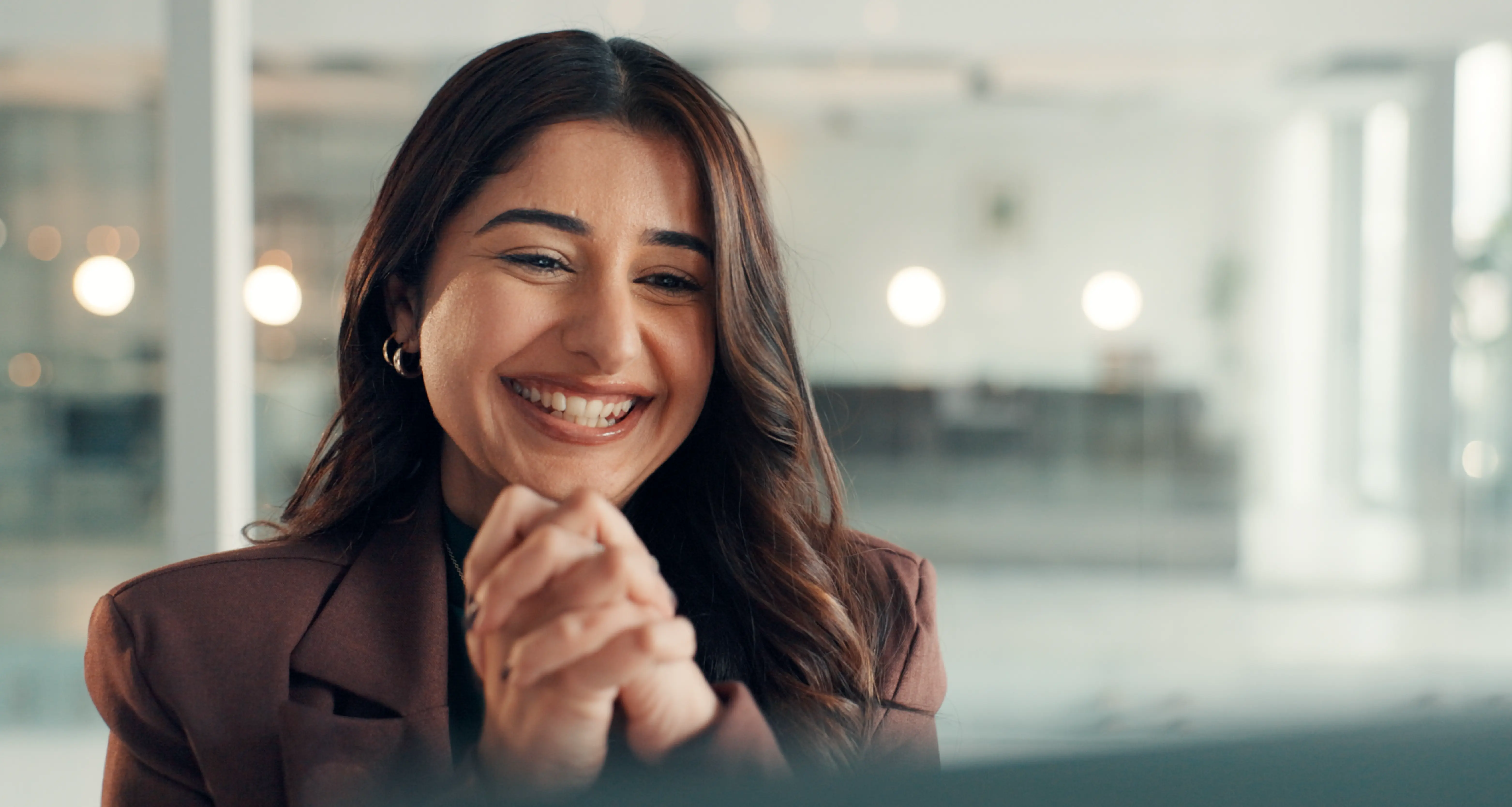 Smiling woman in a brown blazer holding a tablet in a bright modern office environment