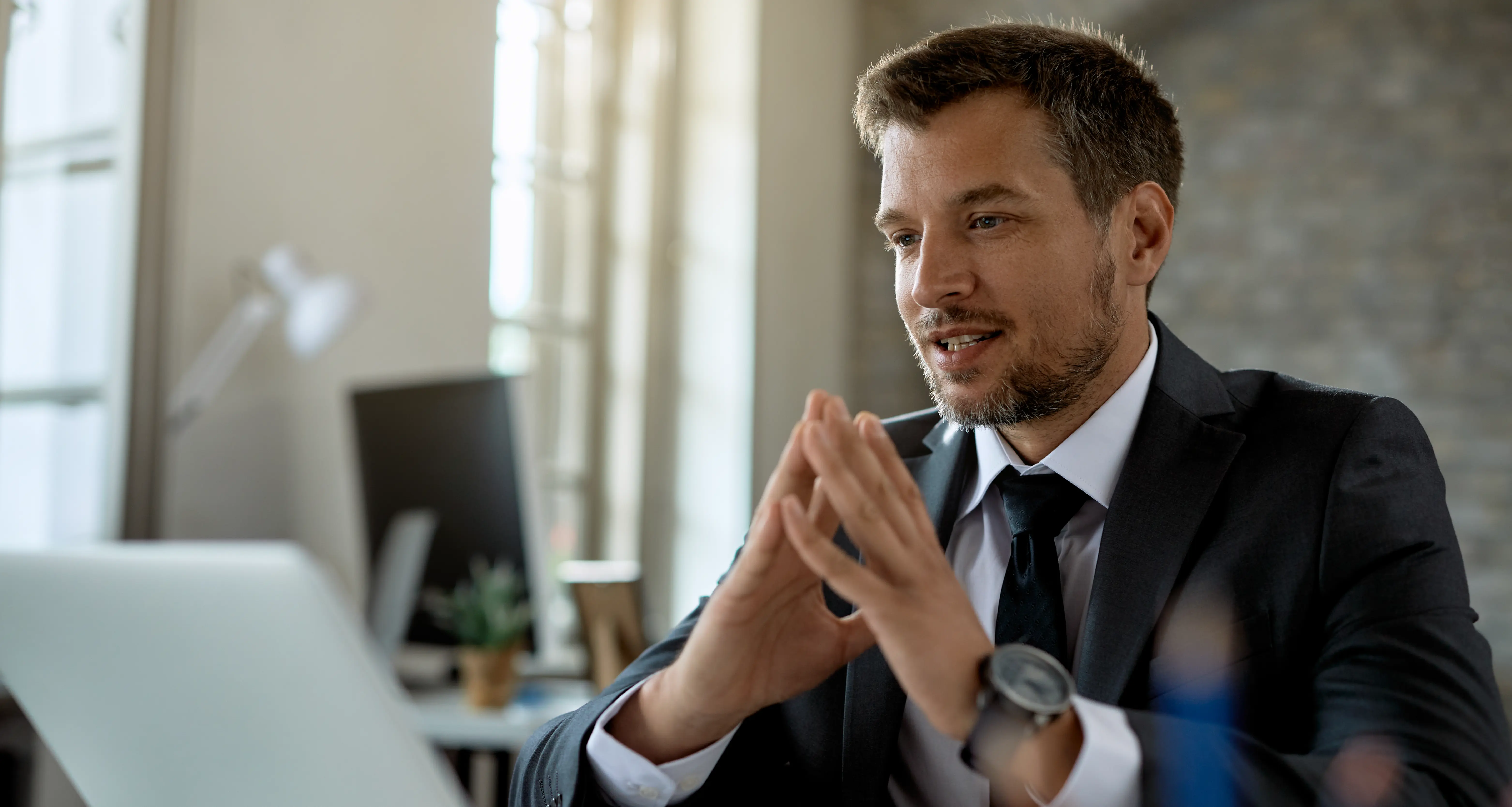 Businessman in a suit gesturing while explaining something on a laptop in a modern office