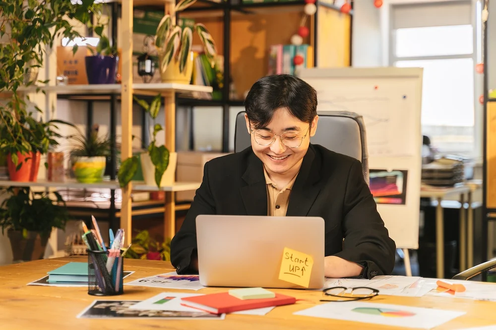 A smiling man sitting at his laptop in a modern office 