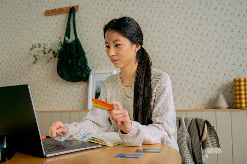 A woman sitting at her desk looking at her laptop holding a credit card in her hand