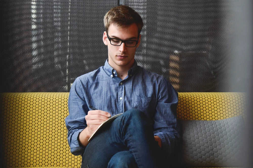 A man with glasses writes something on a notebook