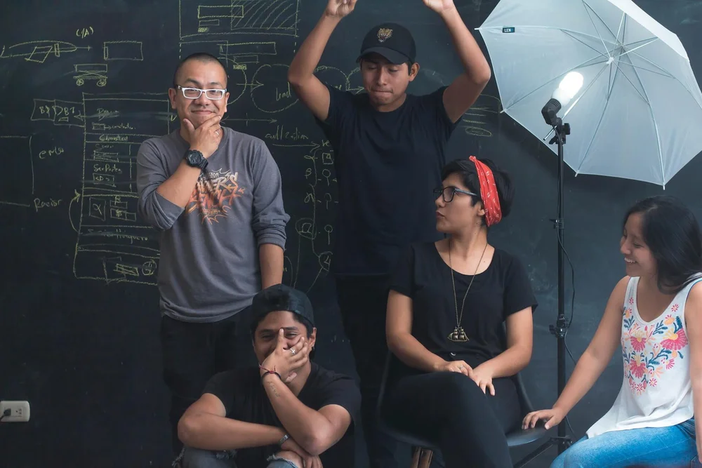 A team in a studio. They're in front of a blackboard, doing funny faces