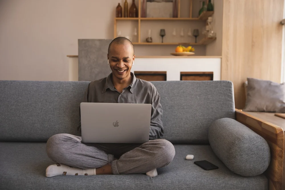 A young Filipino man sitting on a couch with a laptop on his lap